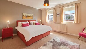A bedroom with a large bed, a red nightstand, a lamp, a window with curtains, and a radiator. - Host Stay Wood Street Cottage (Barnard Castle)