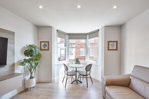 A modern living room with a large window, a dining table with chairs, a sofa, and a potted plant. - Host Stay Berkano The Merchants Quarters (Scarborough)