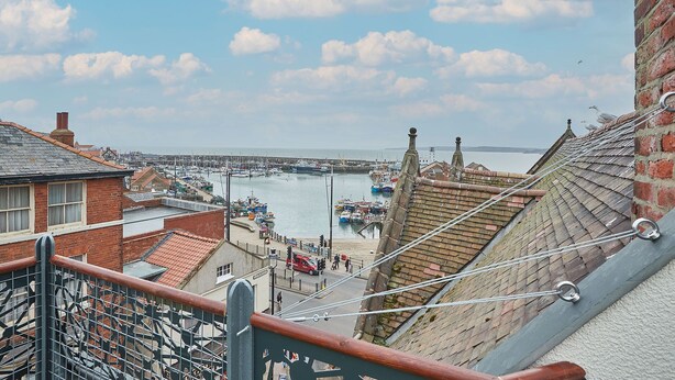 Eine Küstenstadt mit einem Yachthafen, Gebäuden mit roten Ziegeldächern und freiem Blick auf das Meer.