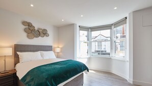 Ein modernes Schlafzimmer mit einem großen Bett, einer Wanddekoration und Blick auf die Straße durch ein Erkerfenster.