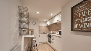 Eine moderne Küche mit Einbauofen, Mikrowelle und Spüle. An der Wand hängt ein Metallregal und darüber eine Uhr.