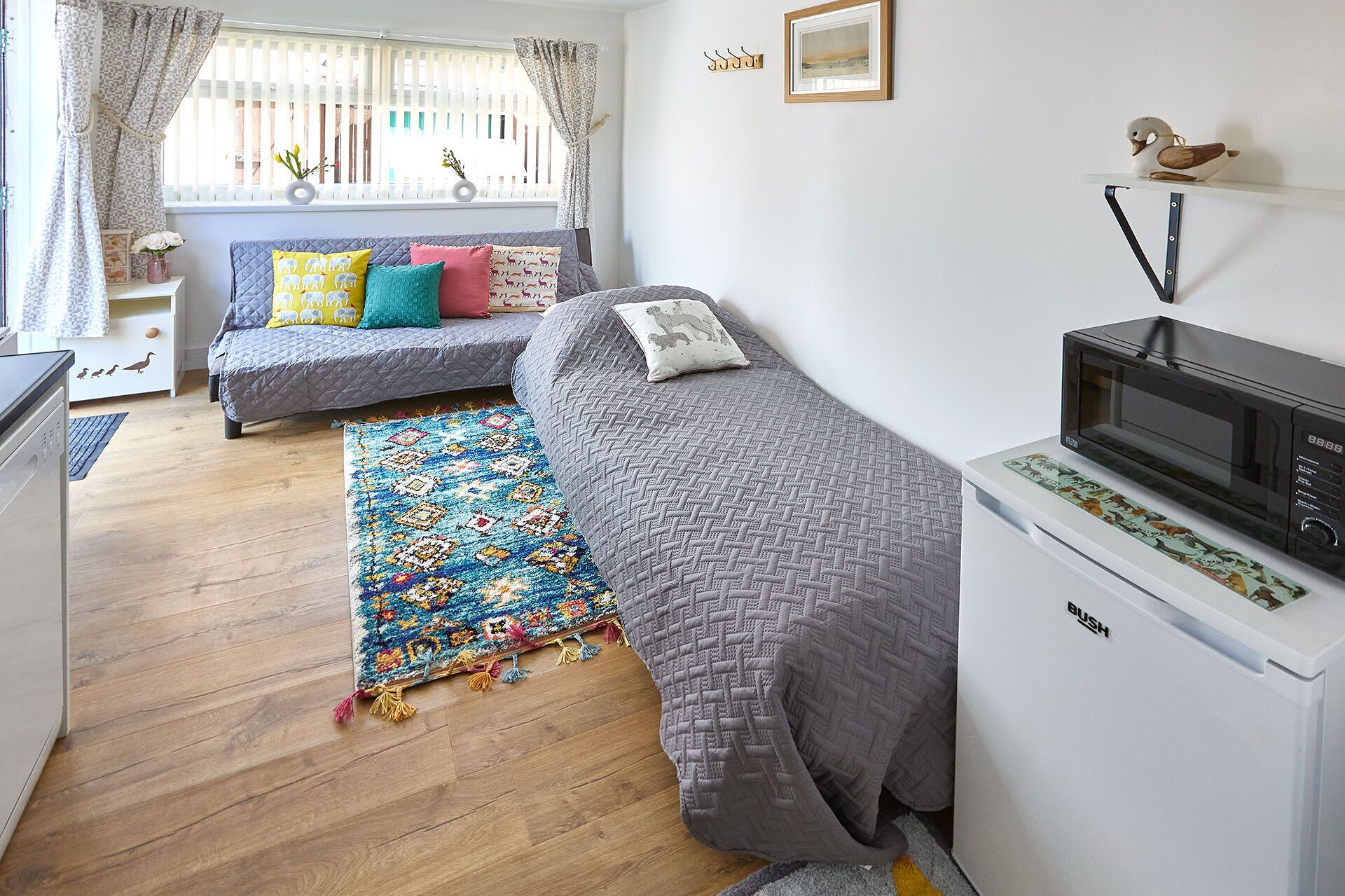 A compact bedroom with a bed, a small desk, a microwave, and a window with curtains.
