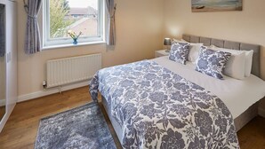 Et soveværelse med en stor seng, et natbord, et vindue med gardiner, en radiator og et billede på væggen.