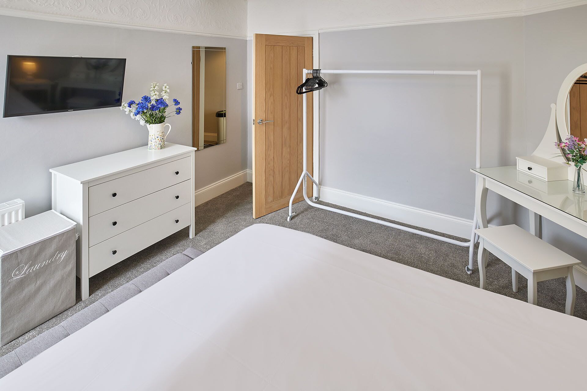 Une chambre à coucher comprenant un lit, une commode, une coiffeuse avec un miroir, une télévision et une porte donnant sur une salle de bain.