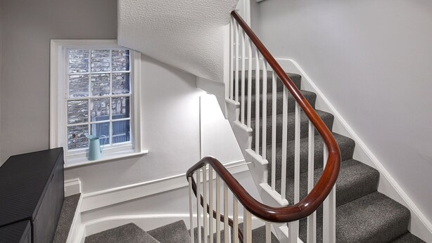 A staircase with a wooden handrail, white railings, and grey carpeted steps.
