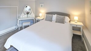 A neatly arranged hotel room with a large bed, two bedside tables with lamps, a small desk with a mirror, and a chair.