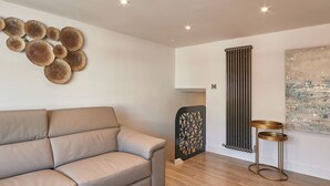 A modern living room with a beige sofa, a decorative wall piece, a radiator, and a small round table. - Host Stay Laguz The Merchants Quarters (Scarborough)