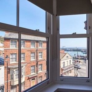 Vista de una bahía desde una ventana, con un puerto, edificios y cielo despejado.