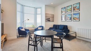 A modern living room with a round table, blue armchairs, and a sofa. There are framed pictures on the wall and a window with blinds. - Host Stay Seaview Retreat (Whitby)