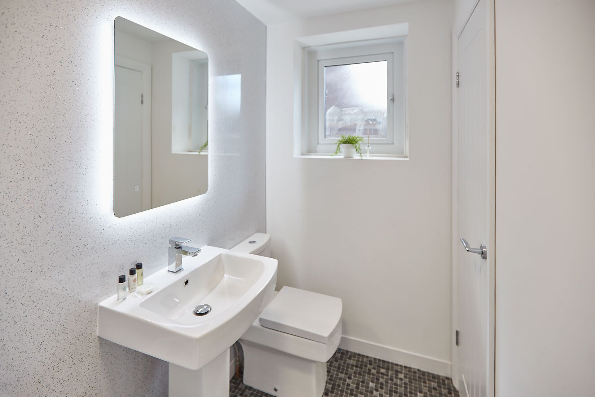 A modern bathroom with a white sink, mirror, and toilet.