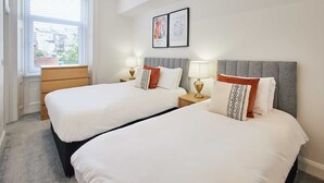 A hotel room with two beds, a wooden dresser, bedside lamps, and a window with blinds. - Host Stay Seaview Retreat (Whitby)