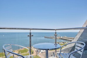 A balcony with a glass railing overlooking a coastal view, including a pier and a body of water.