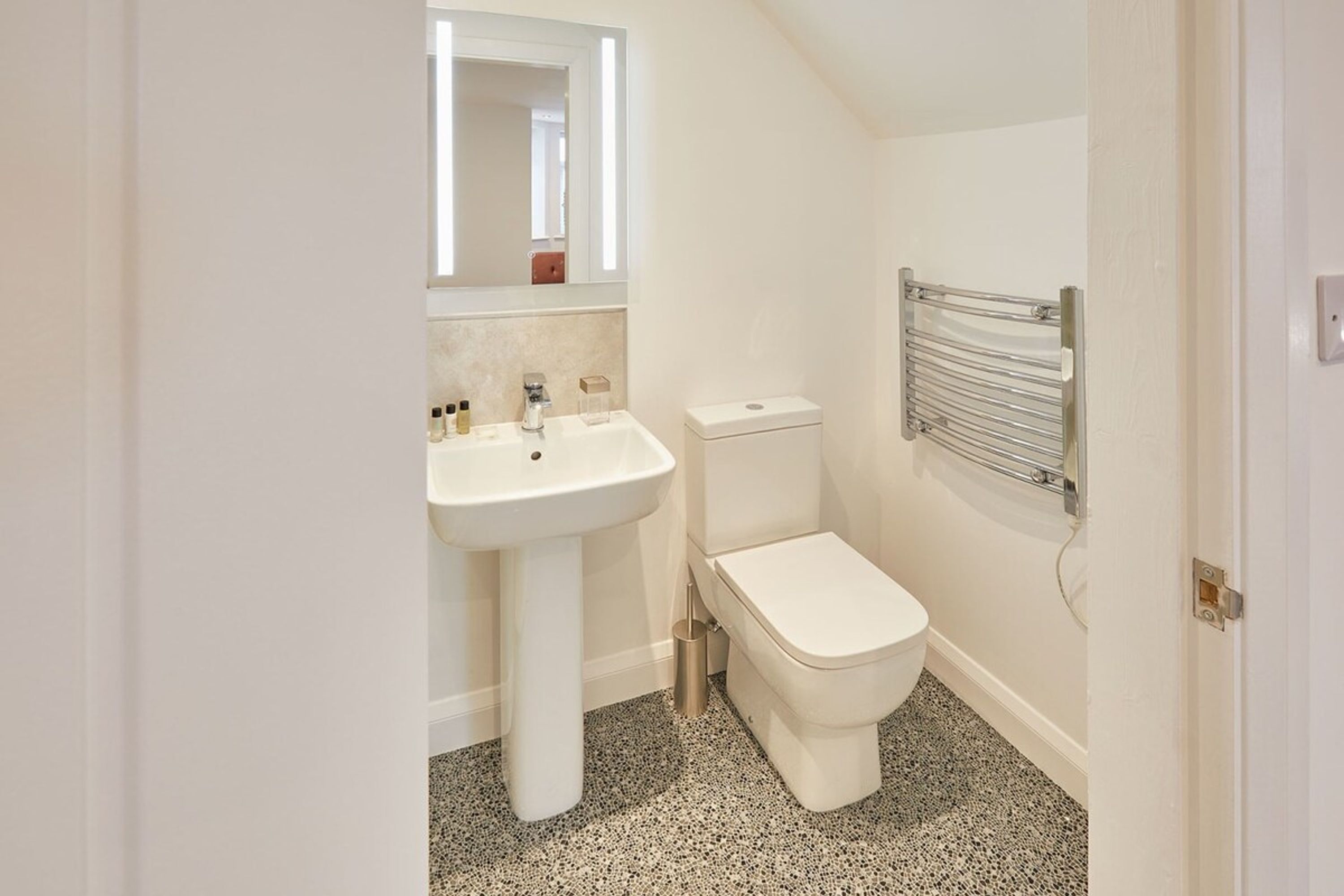 Ein kleines, modernes Badezimmer mit Waschbecken, Toilette und einem Handtuchhalter an der Wand.