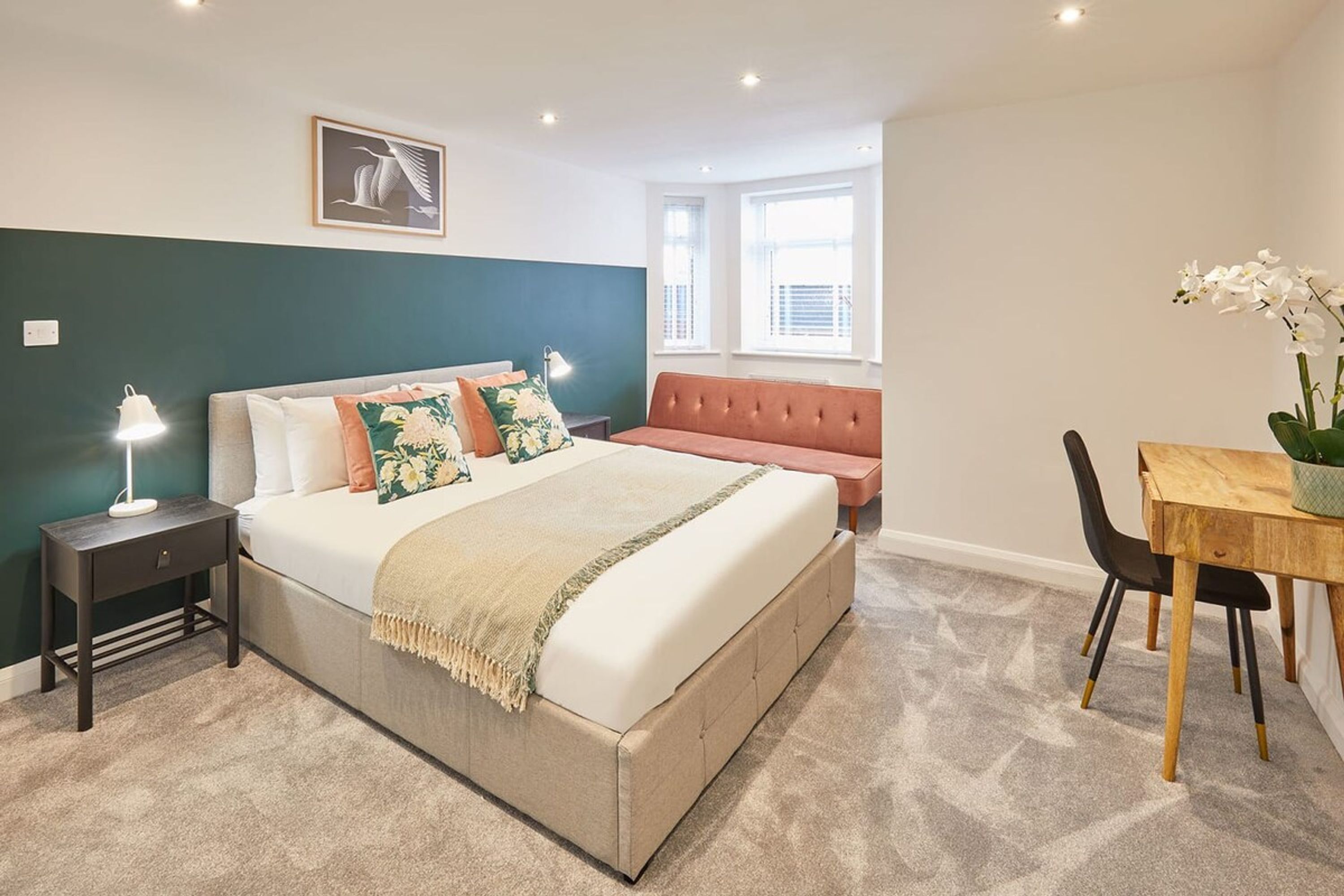 A bedroom with a bed, bedside table, lamp, bench, and a dining area with a table and chairs.