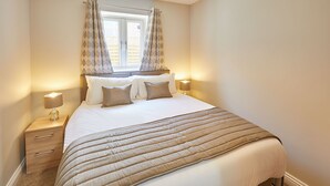 A bedroom with a bed, two bedside tables, a window with curtains, and a ceiling light. - Host Stay Sunny Dale Cottage (Pickering)