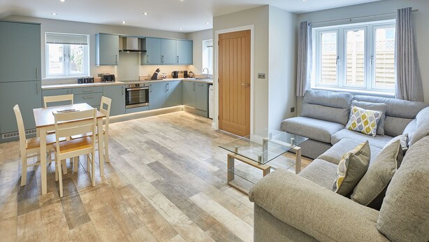 A modern kitchen with grey cabinets, a wooden door, and a dining area with a glass table. - Host Stay Sunny Dale Cottage (Pickering)