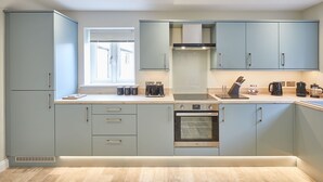 A modern kitchen with grey cabinets, a built-in oven, and a window with blinds. - Host Stay Sunny Dale Cottage (Pickering)