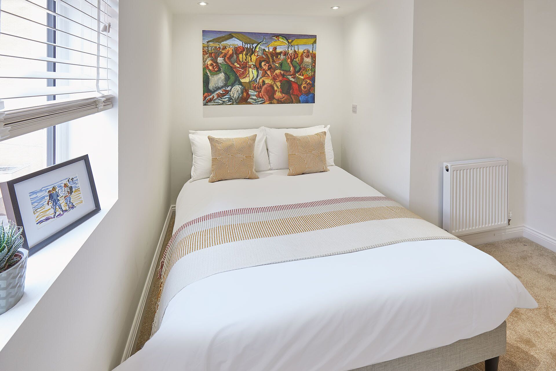 A bedroom with a bed, a framed picture on the wall, and a window with blinds.