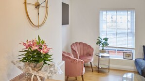 A living room with a round wall clock, a pink armchair, a small round table, and a potted plant. - Host Stay Licence to Chill (Saltburn-by-the-Sea)