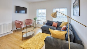 A modern living room with a grey sofa, pink chairs, a yellow rug, and a floor lamp. - Host Stay Licence to Chill (Saltburn-by-the-Sea)