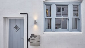 A building with a grey door, a window with multiple panes, and a wall-mounted light fixture. - Host Stay 11 Bakehouse Yard (Whitby)