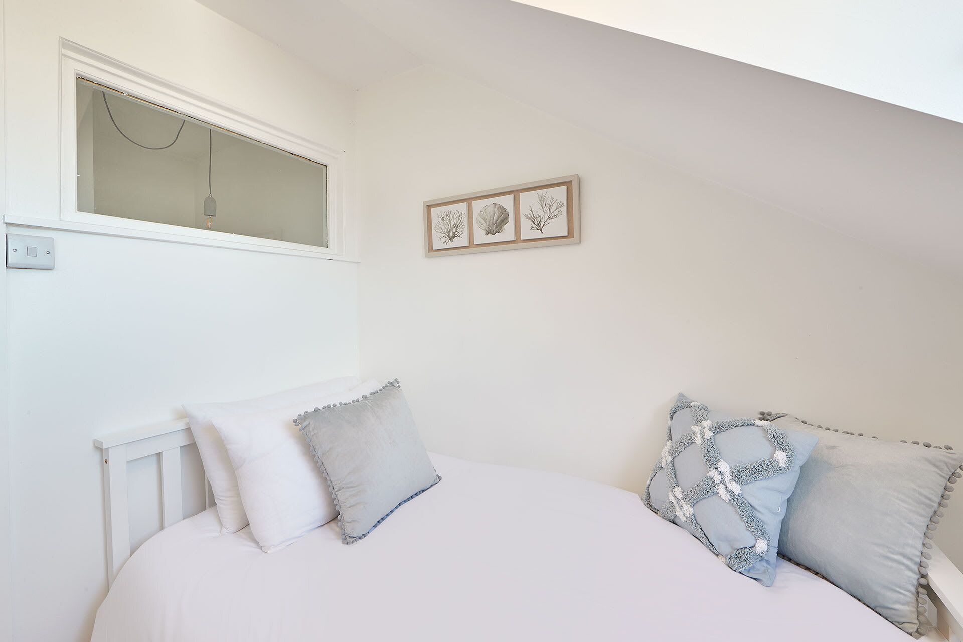 Une chambre à coucher avec un lit, deux oreillers, une fenêtre et un tableau encadré au mur.