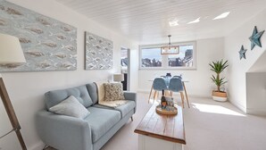 Un salon moderne avec un canapé bleu clair, une table basse en bois et une vue sur la ville par une grande fenêtre.