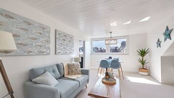 A modern living room with a light blue sofa, a wooden coffee table, and a city view through a large window.
