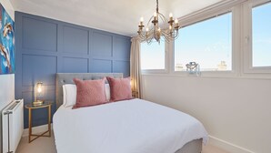 Une chambre à coucher avec un grand lit, un lustre, une vue sur la ville et un mur d’accent bleu.
