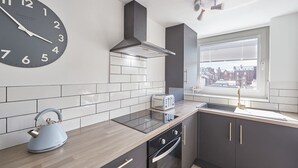 Une cuisine moderne avec une grande horloge murale, une bouilloire, un grille-pain et une fenêtre donnant sur la ville.