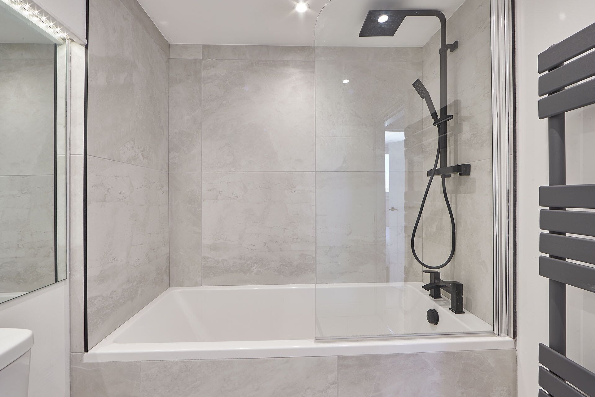 A modern bathroom with a glass-enclosed shower, a white bathtub, and a large mirror.
