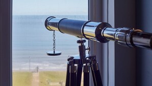 A telescope mounted on a tripod by a window overlooking a body of water. - Host Stay Sea Watcher (Whitby)