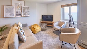 A modern living room with a sofa, two armchairs, a coffee table, and a TV. There are framed artworks on the wall, a potted plant, and a tripod. - Host Stay Sea Watcher (Whitby)