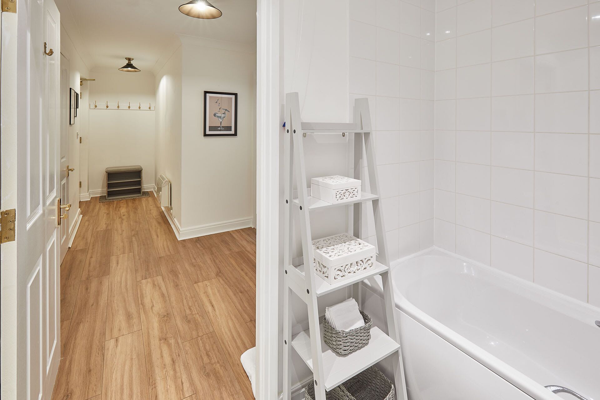 Une salle de bain avec une baignoire blanche, une étagère blanche avec des paniers et un plancher en bois.