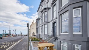 Reihle grau getaner Stadtäuser mit weißen Fensterrahmen, eine hölzerne Bank und eine 'SLOW'-Beschilderung auf der Straße.