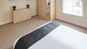 A bedroom with a bed, a wooden wardrobe, a mirror, and two wall-mounted speakers. - Host Stay 1 Oswy Street (Whitby)