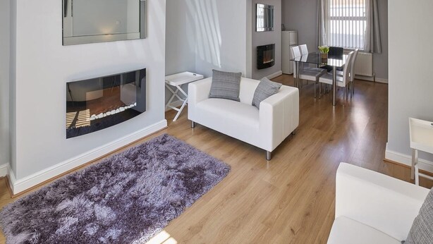A modern living room with a white sofa, a fireplace, and a dining area with a table and chairs. - Host Stay 1 Oswy Street (Whitby)