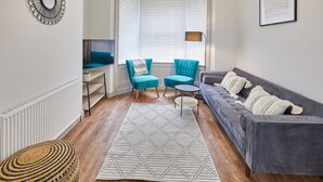 Una sala de estar moderna con un sofá gris, sillones color turquesa, una mesita redonda y una alfombra estampada.