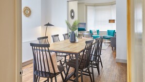 Comedor con mesa de madera, sillas negras, una planta en maceta y ventana con persianas.