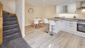 A modern kitchen with white cabinets, a wooden staircase, and a dining area with white chairs. - Host Stay The Cottage Bagdale Hall (Whitby)