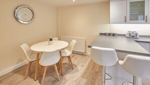 A modern kitchen with a round table and bar stools, a built-in oven, and a mirrored wall clock. - Host Stay The Cottage Bagdale Hall (Whitby)