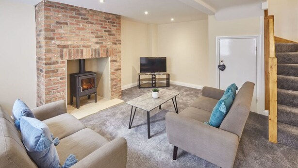 A living room with a brick fireplace, a TV on a stand, and a staircase. - Host Stay The Cottage Bagdale Hall (Whitby)
