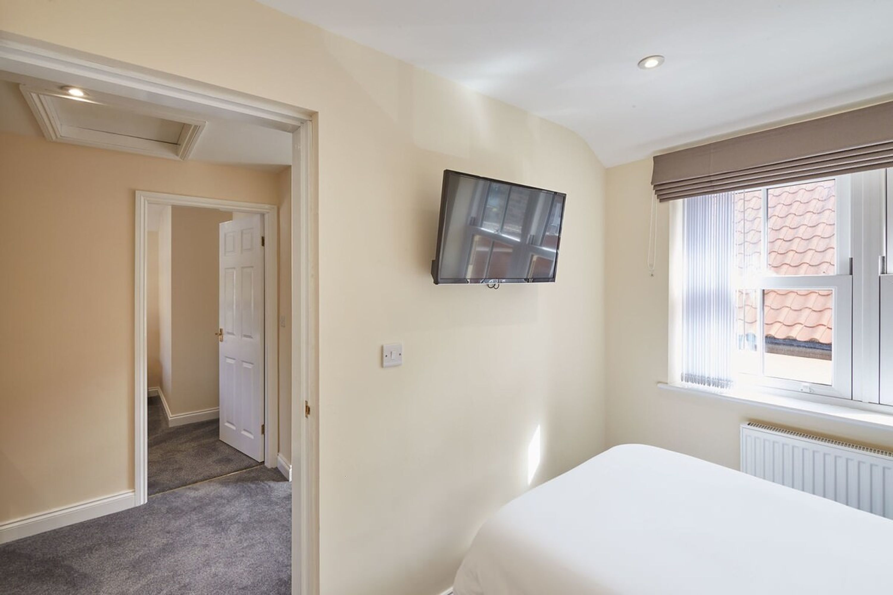 Un dormitorio con una cama, un televisor montado en la pared y una ventana con persianas.