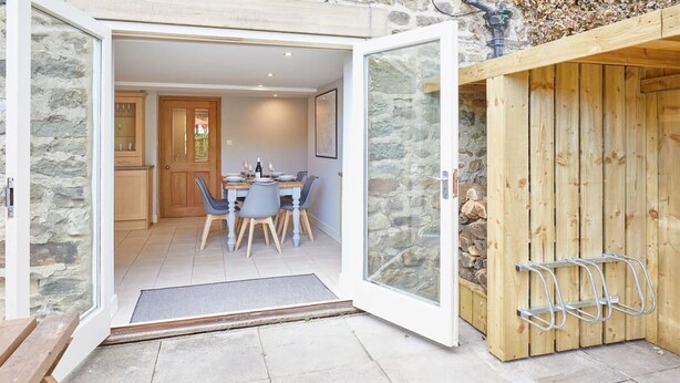 Une façade en pierre avec une porte en bois donnant sur un espace repas comprenant une table et des chaises.