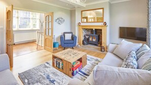 Un salon comprenant un canapé, une table basse avec des livres, une cheminée, un téléviseur et une grande fenêtre avec des stores.