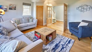 Un salon avec un canapé, un fauteuil bleu, une table basse avec des jouets et un lustre.