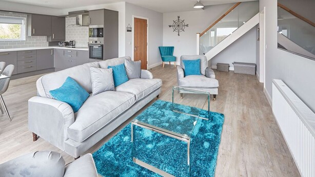 A modern living room with a grey sofa, a blue armchair, and a glass coffee table. - Host Stay Badgers Cottage (Saltburn-by-the-Sea)