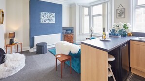 A modern kitchen with a central island, a dining area with a blue sofa, and a living space with a TV and decorative items.