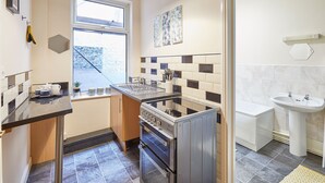 A compact kitchen with a stove, oven, and sink, a window with a view, and a tiled backsplash. - Host Stay Ocean Breeze (Scarborough)