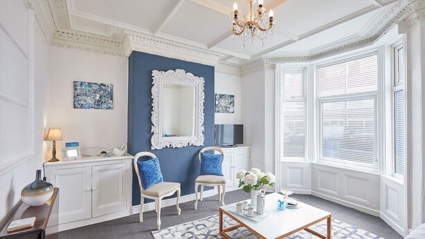 A room with a blue accent wall, a white fireplace, two chairs, a coffee table, and a large window with blinds. - Host Stay Ocean Breeze (Scarborough)